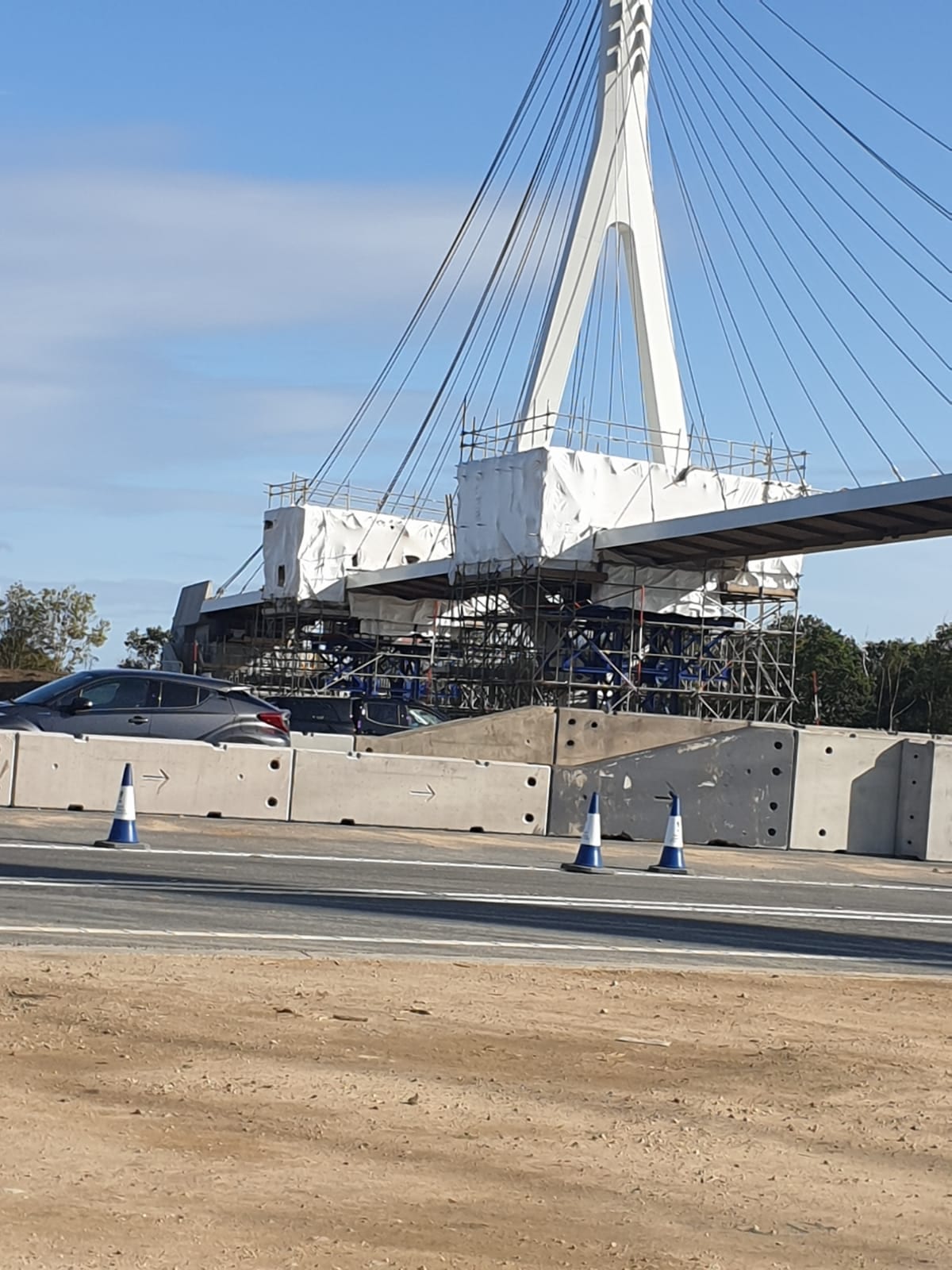 Roadside scaffolding and concrete barriers on a highway alongside a cable-stayed bridge