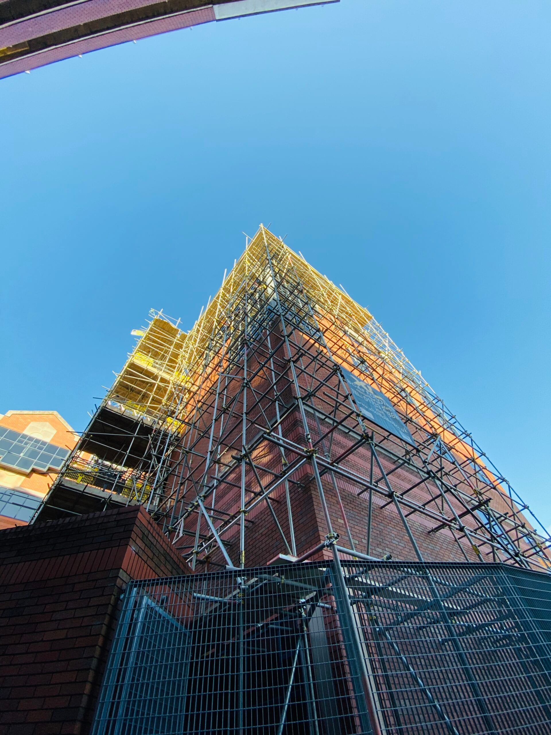 Tall façade scaffold clad in debris netting against a clear sky