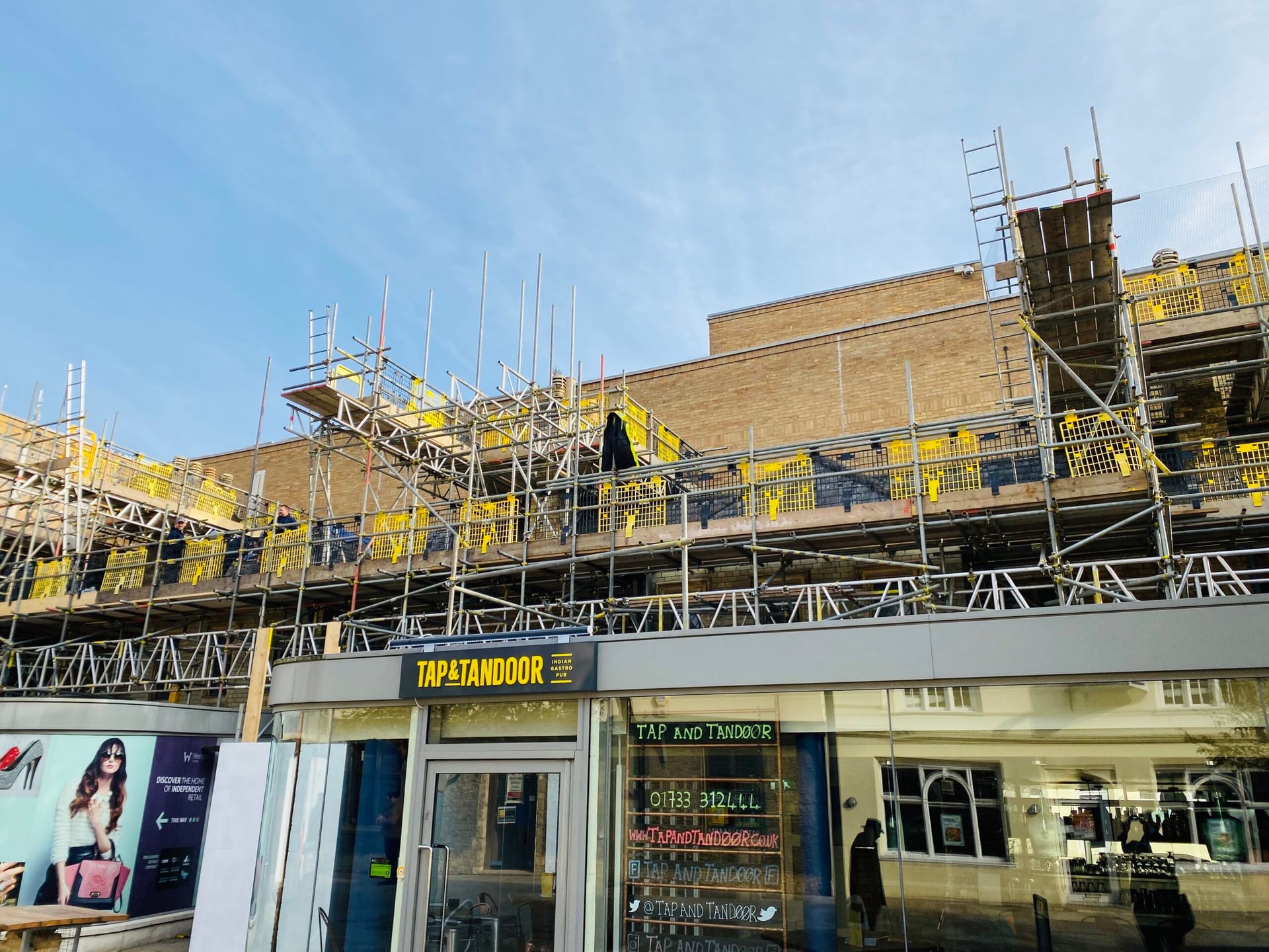 Scaffold erected above an occupied retail parade, with shopfronts trading at street level below