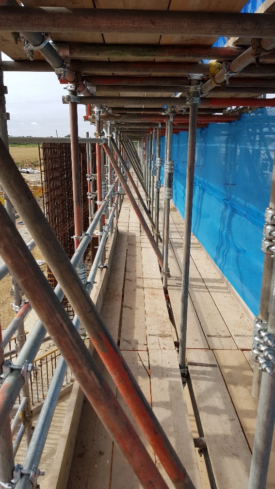 Close view of scaffold tube and fittings erected in a narrow gap between a building elevation and blue protective sheeting
